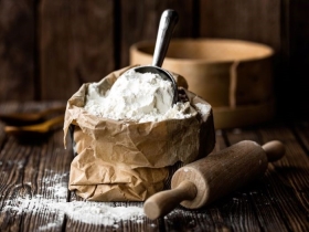 A bag of flour on a wooden table beside a rolling pin